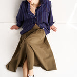 Woman wearing a blue shirt and brown skirt sitting on a white floor.