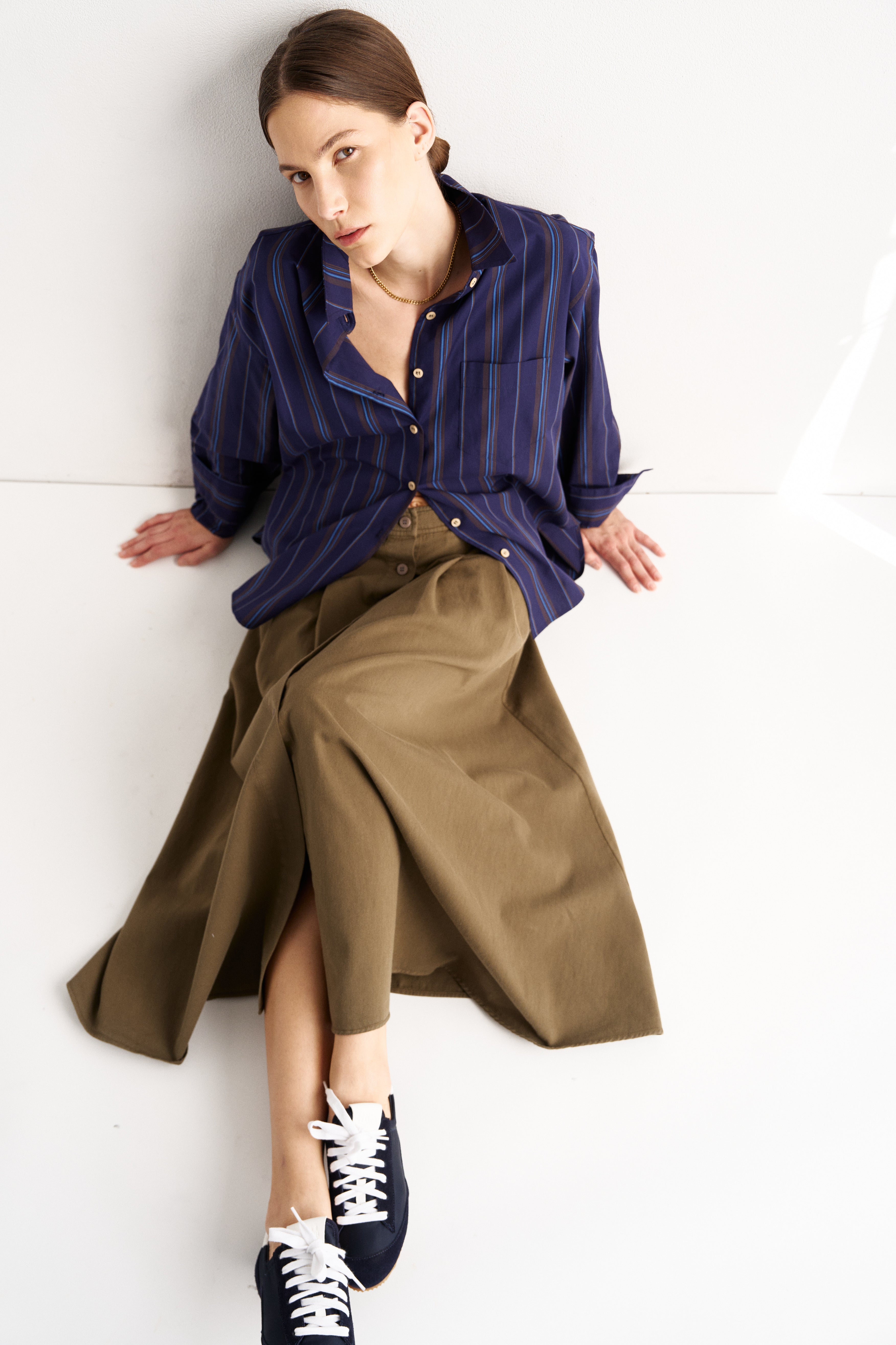 Woman wearing a blue shirt and brown skirt sitting on a white floor.