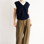 Person wearing a navy sleeveless top and beige pants on a white background