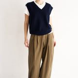 Person wearing a navy sleeveless top and beige pants on a white background