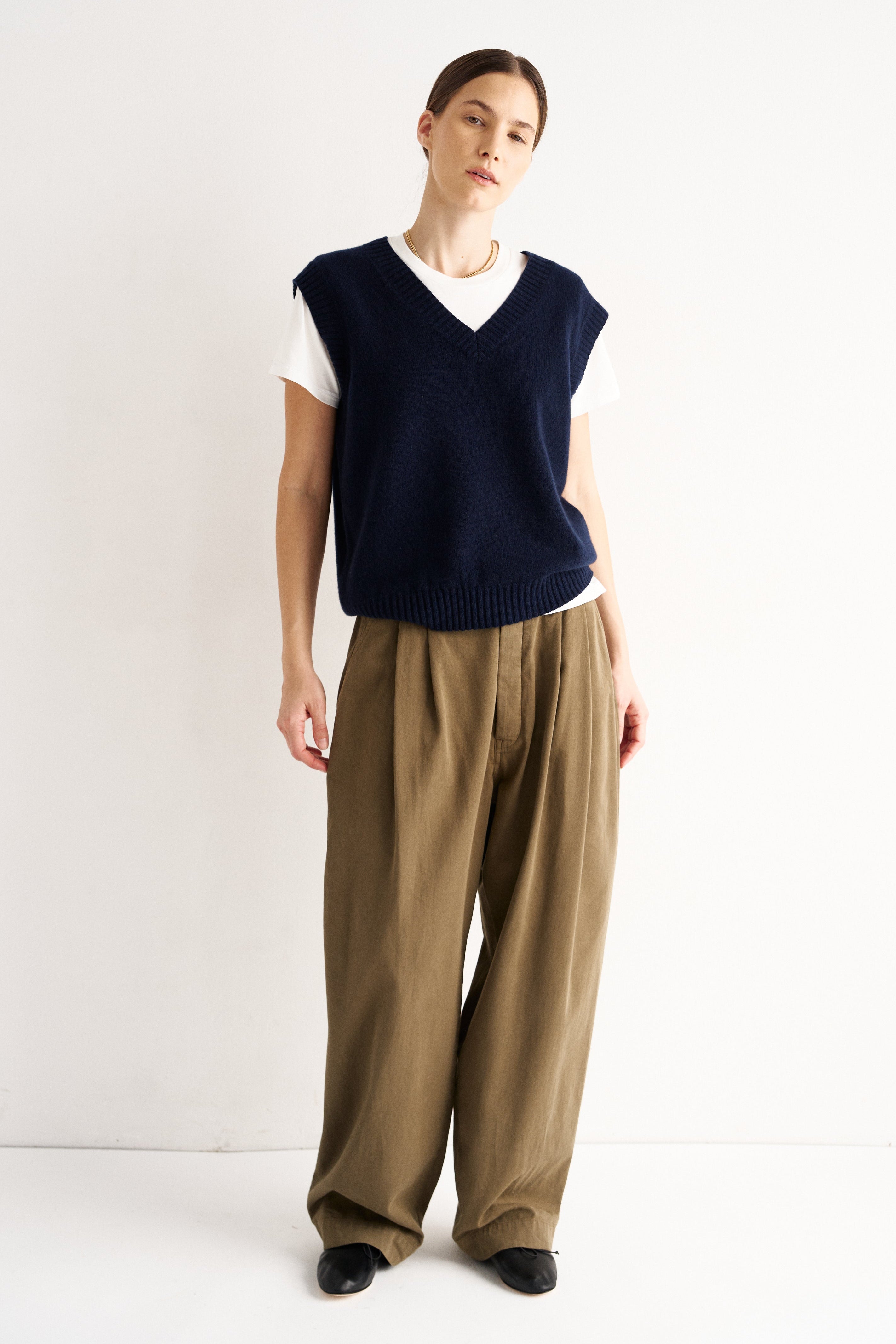 Person wearing a navy sleeveless top and beige pants on a white background