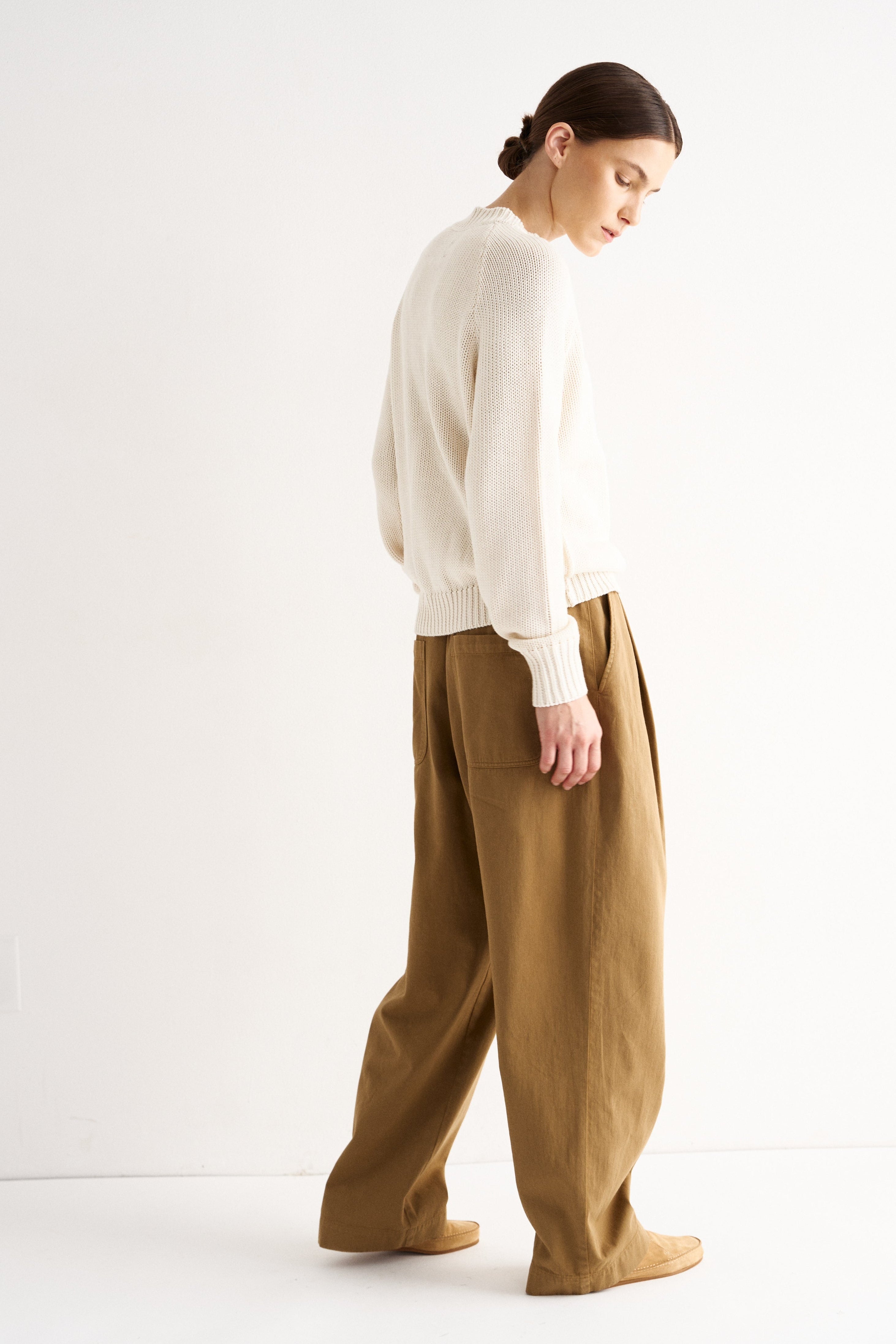 Woman wearing a white sweater and brown pants on a white background
