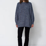 woman standing in front of a white will in a crewneck sweater
