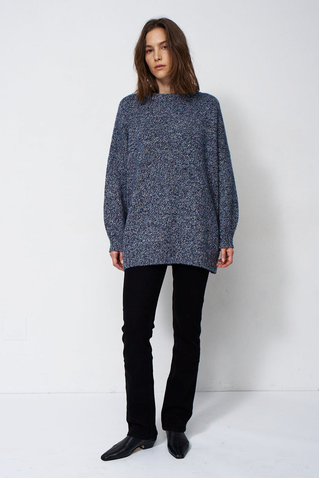 woman standing in front of a white will in a crewneck sweater