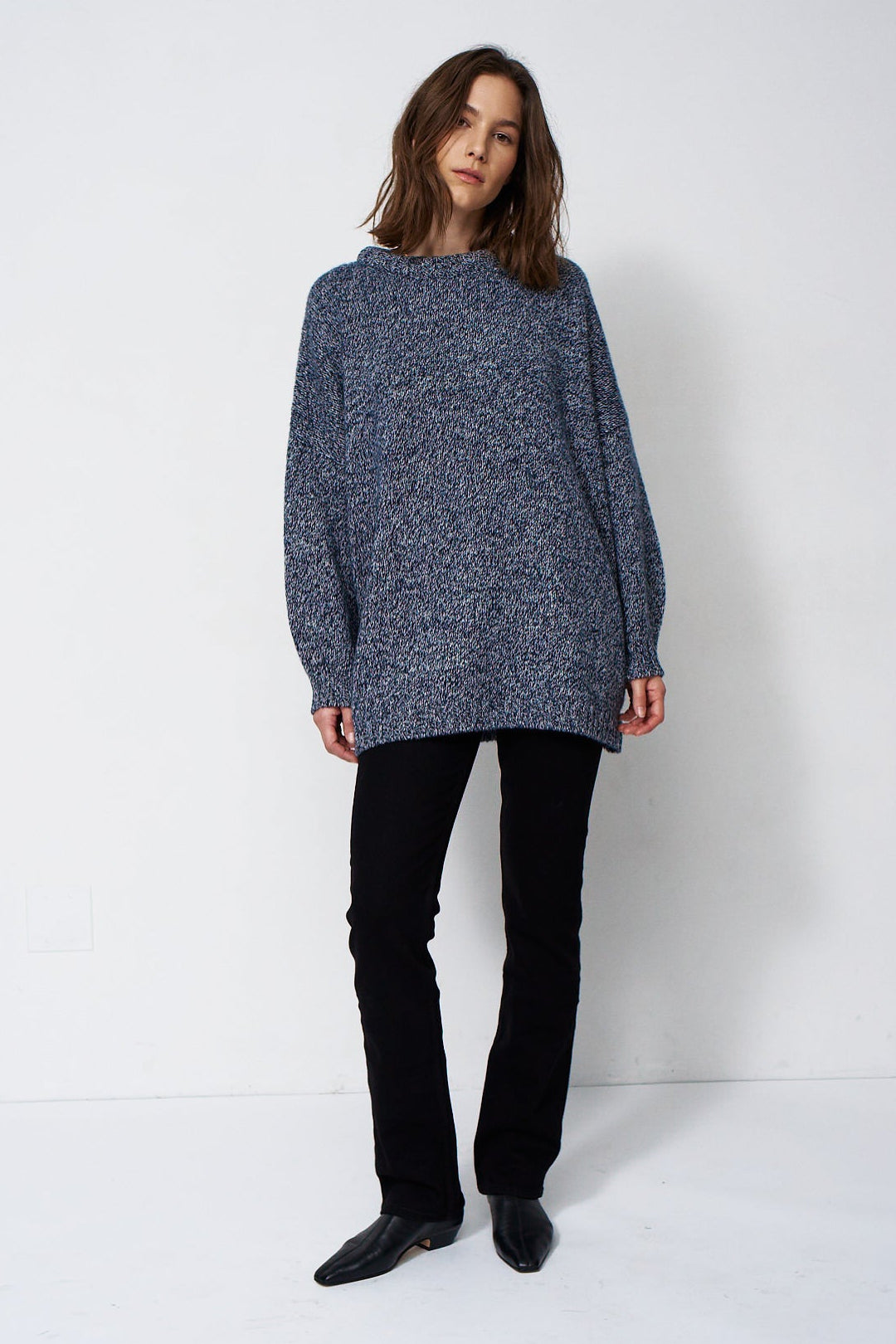 woman standing in front of a white will in a crewneck sweater
