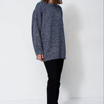 woman standing in front of a white will in a crewneck sweater