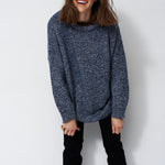 woman standing in front of a white will in a crewneck sweater
