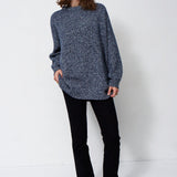 woman standing in front of a white will in a crewneck sweater