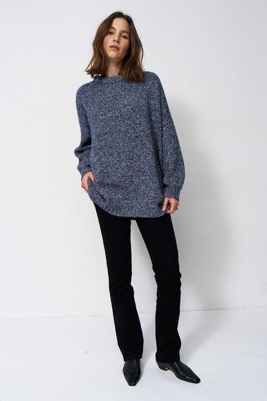 woman standing in front of a white will in a crewneck sweater
