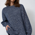 woman standing in front of a white will in a crewneck sweater
