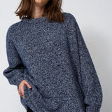 woman standing in front of a white will in a crewneck sweater