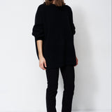 model wearing all black standing in front of a white wall