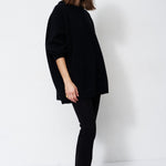 model wearing all black standing in front of a white wall