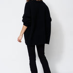 model wearing all black standing in front of a white wall