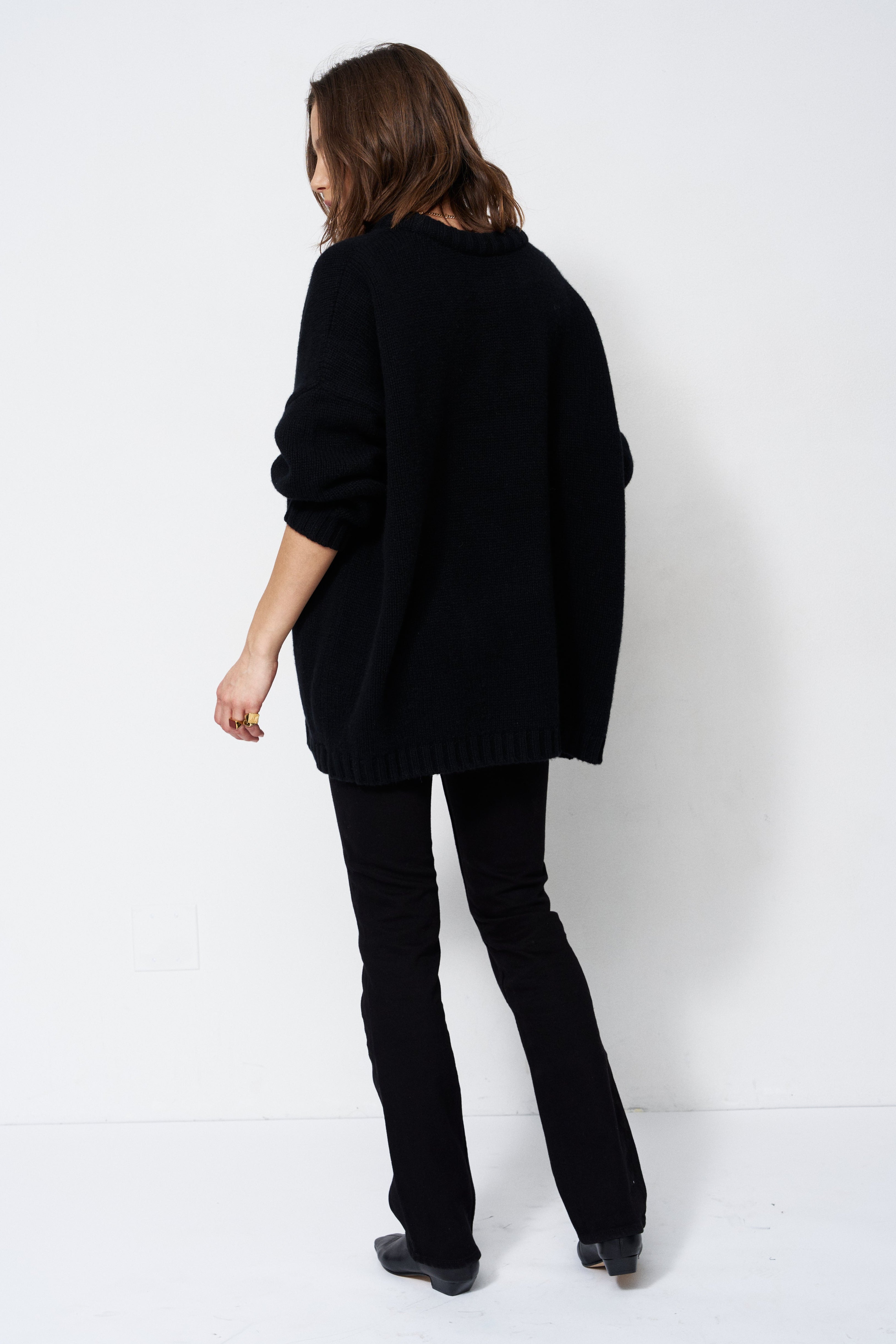 model wearing all black standing in front of a white wall