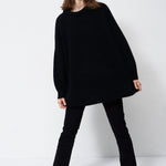 model wearing all black standing in front of a white wall