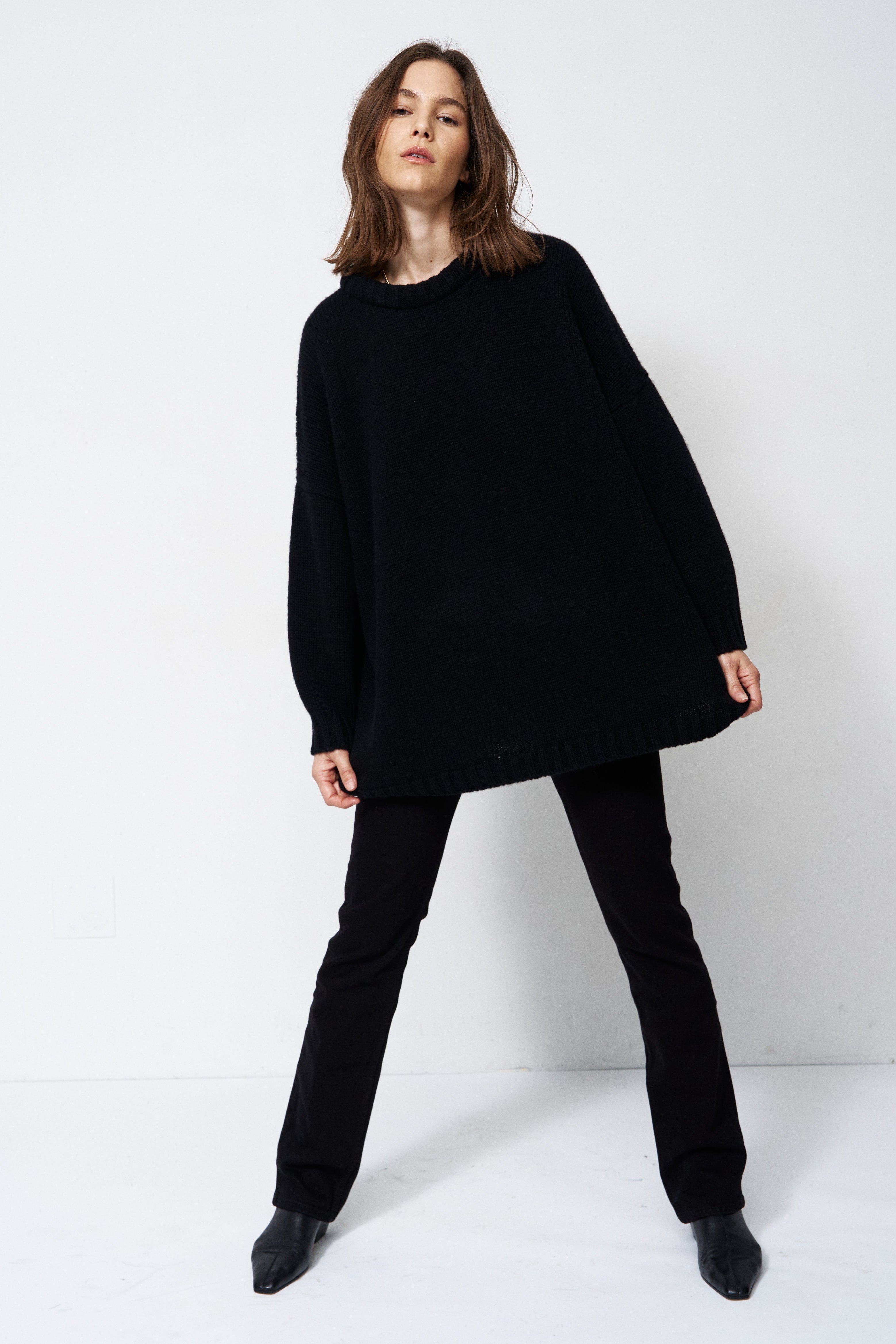 model wearing all black standing in front of a white wall