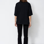 A model viewed from the back wearing an oversized black short-sleeve top and black flared pants against a plain white studio background.