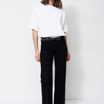 A woman modeling a white short-sleeve top and black wide-leg trousers with a black belt, standing against a plain white studio background.