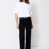 A woman modeling a white short-sleeve top and black wide-leg trousers with a black belt, standing against a plain white studio background.