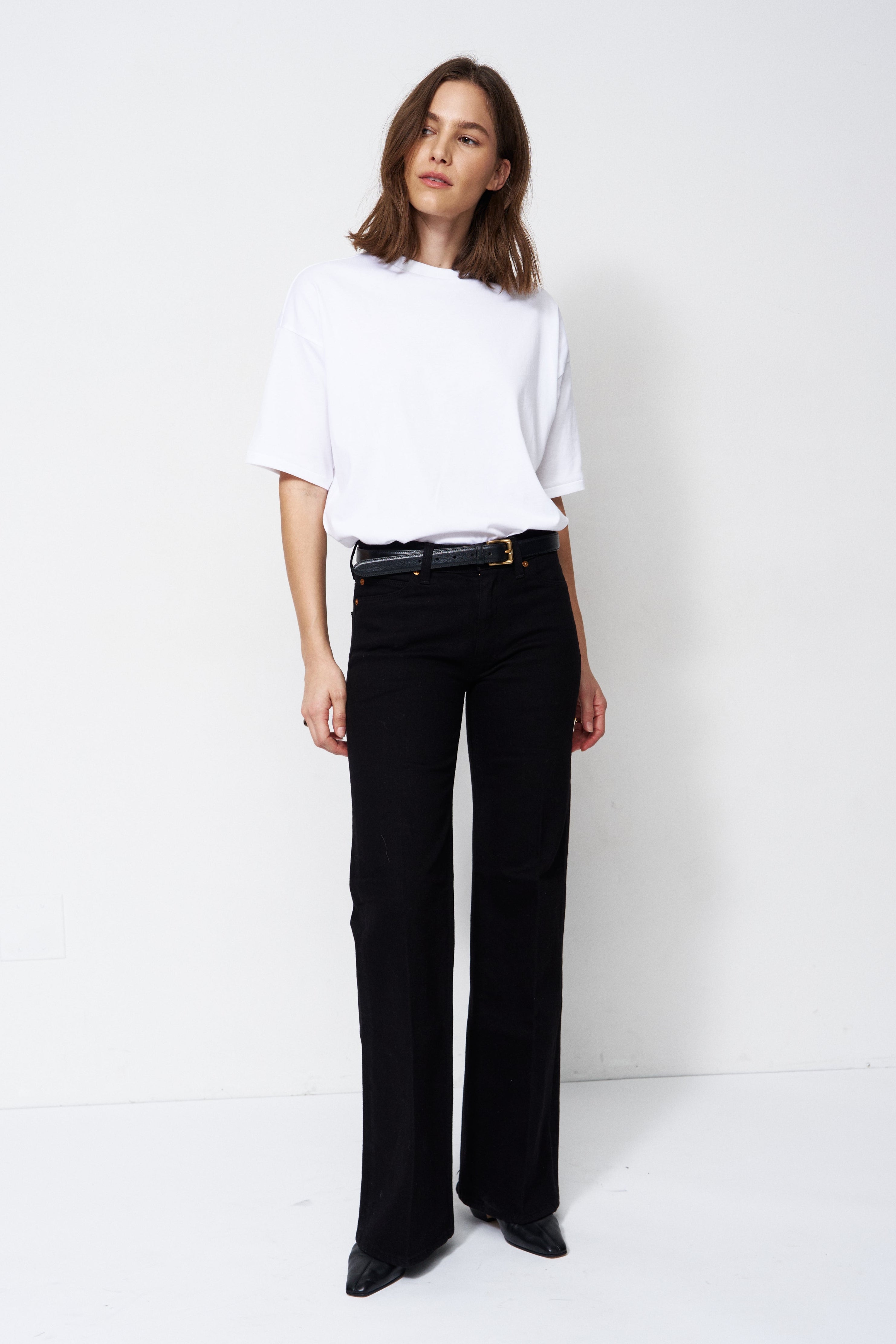A woman modeling a white short-sleeve top and black wide-leg trousers with a black belt, standing against a plain white studio background.