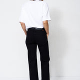 A model shown from the back wearing a white t-shirt and black wide-leg trousers, standing against a plain white studio background.