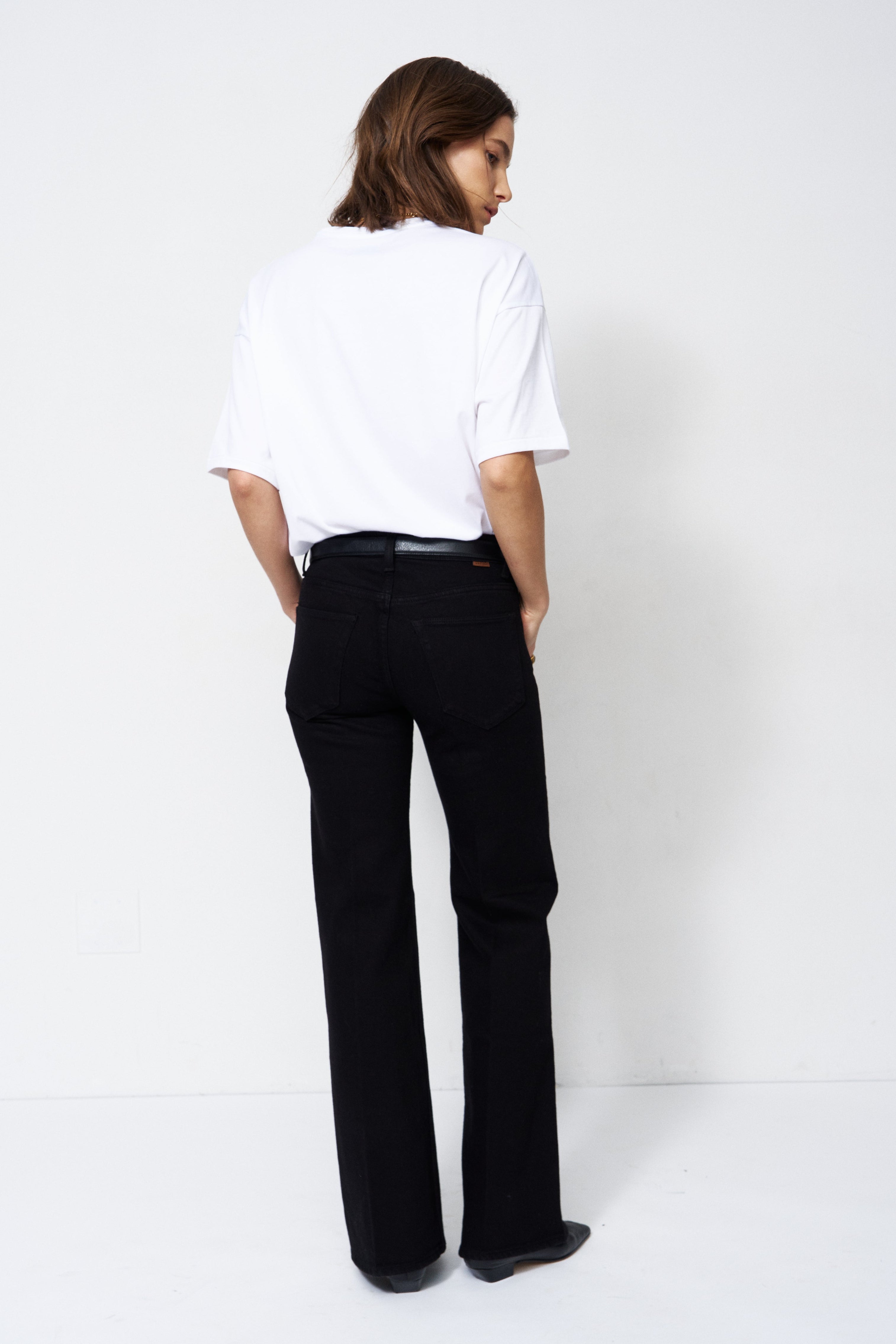 A model shown from the back wearing a white t-shirt and black wide-leg trousers, standing against a plain white studio background.