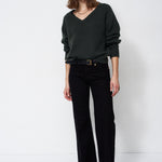 A woman modeling a dark green V-neck knit sweater and black wide-leg trousers with a black belt, standing against a plain white studio background.