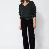 A woman modeling a dark green V-neck knit sweater and black wide-leg trousers with a black belt, standing against a plain white studio background.