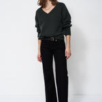 A woman modeling a dark green V-neck knit sweater and black wide-leg trousers with a black belt, standing against a plain white studio background.