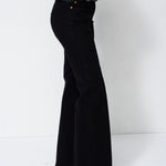 A person wearing black wide-leg flared pants, a dark green sweater, and black pointed shoes, shown from the waist down against a plain white studio background.