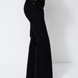 A person wearing black wide-leg flared pants, a dark green sweater, and black pointed shoes, shown from the waist down against a plain white studio background.