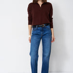 A woman modeling a dark brown long-sleeve polo-neck knit top and blue straight-leg jeans against a plain white studio background.