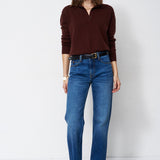 A woman modeling a dark brown long-sleeve polo-neck knit top and blue straight-leg jeans against a plain white studio background.