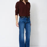 A woman modeling a dark brown long-sleeve polo shirt and blue wide-leg jeans against a plain white studio background.
