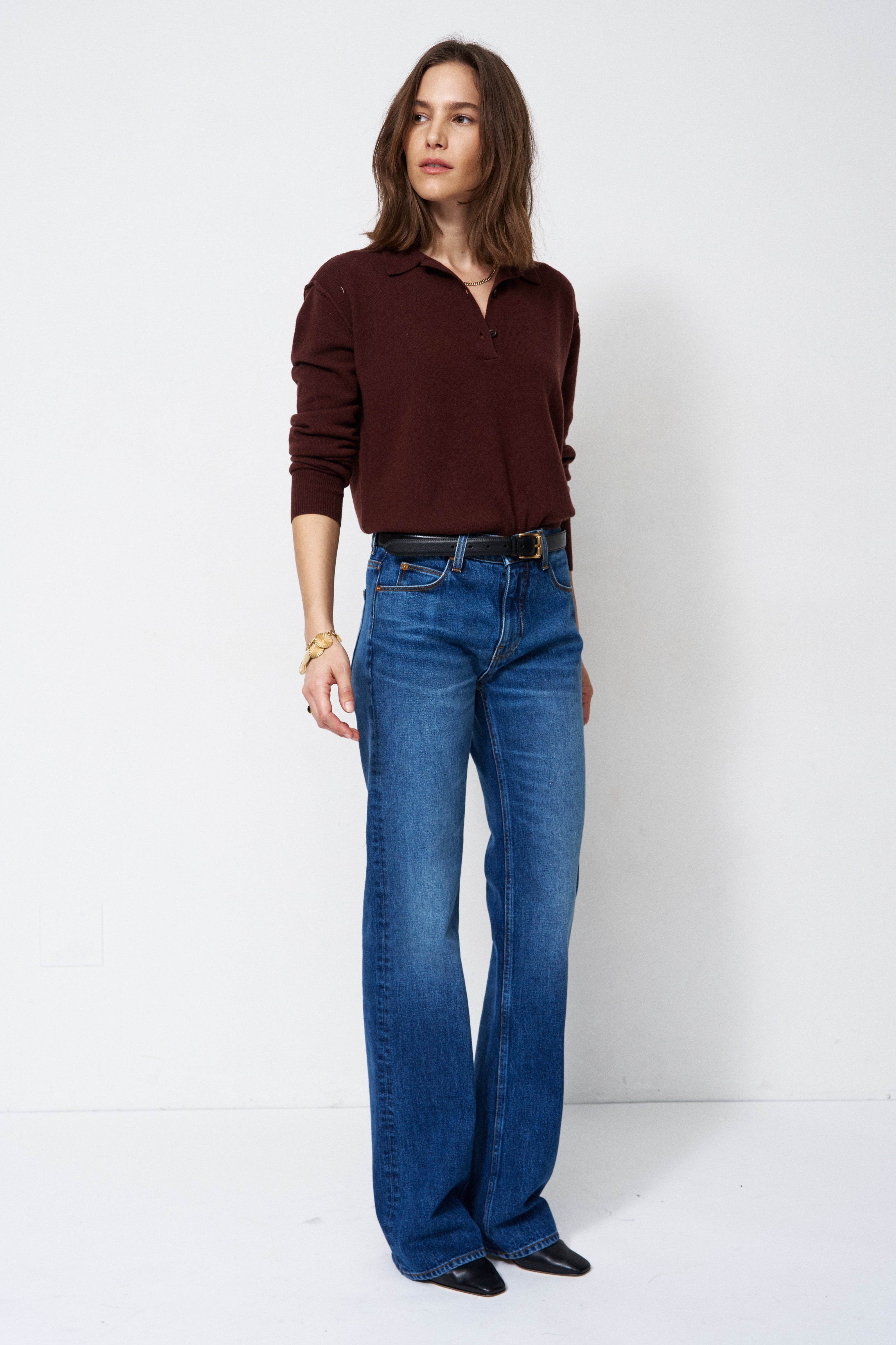 A woman modeling a dark brown long-sleeve polo shirt and blue wide-leg jeans against a plain white studio background.