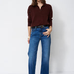 A woman modeling a dark brown long-sleeve polo shirt and blue wide-leg jeans against a plain white studio background.