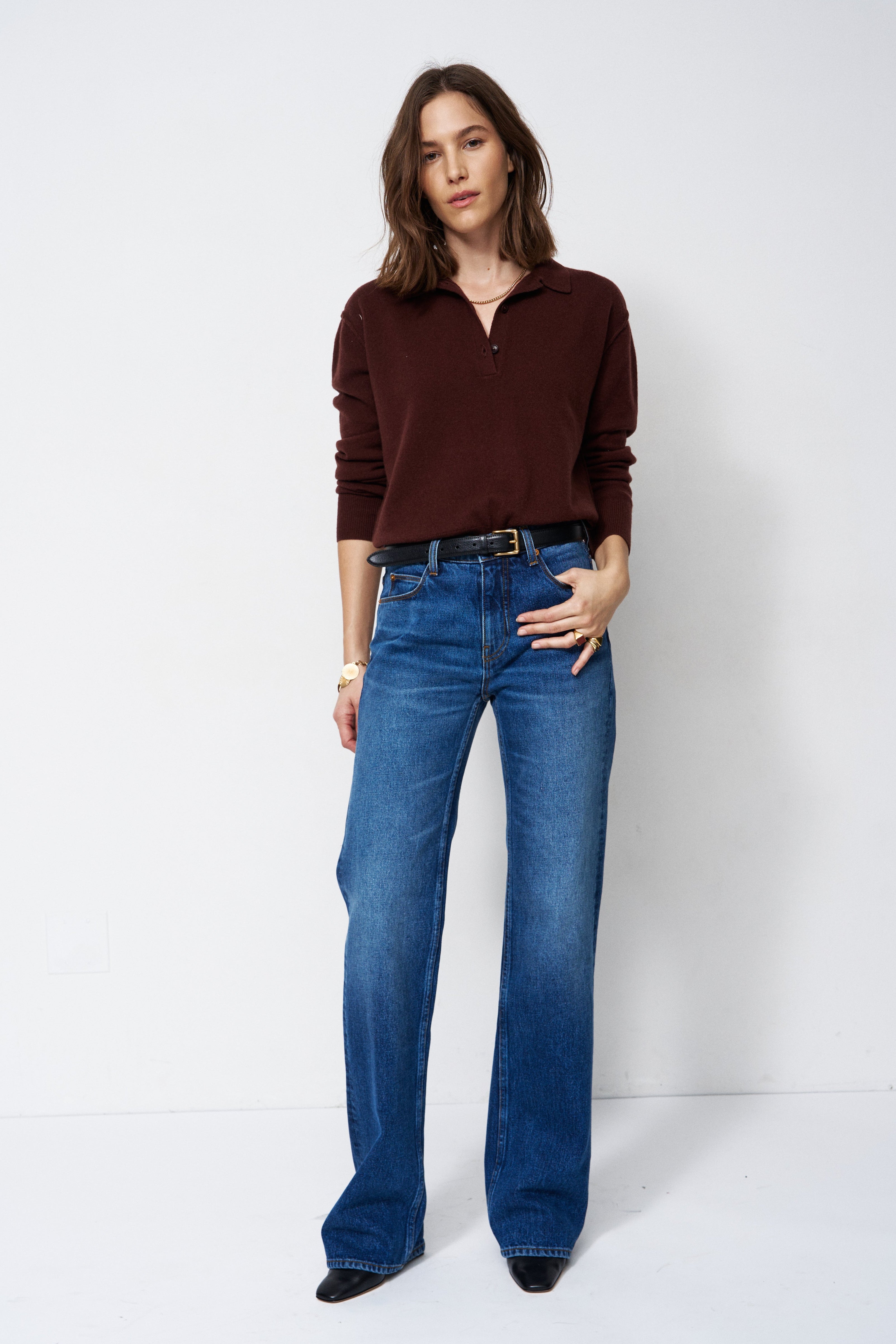 A woman modeling a dark brown long-sleeve polo shirt and blue wide-leg jeans against a plain white studio background.