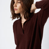 A woman wearing a dark brown long-sleeve knit polo shirt with a partial button placket, paired with blue jeans, photographed against a clean white studio background.