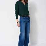 A woman modeling a dark green long-sleeve knit top and blue wide-leg jeans against a plain white studio background.