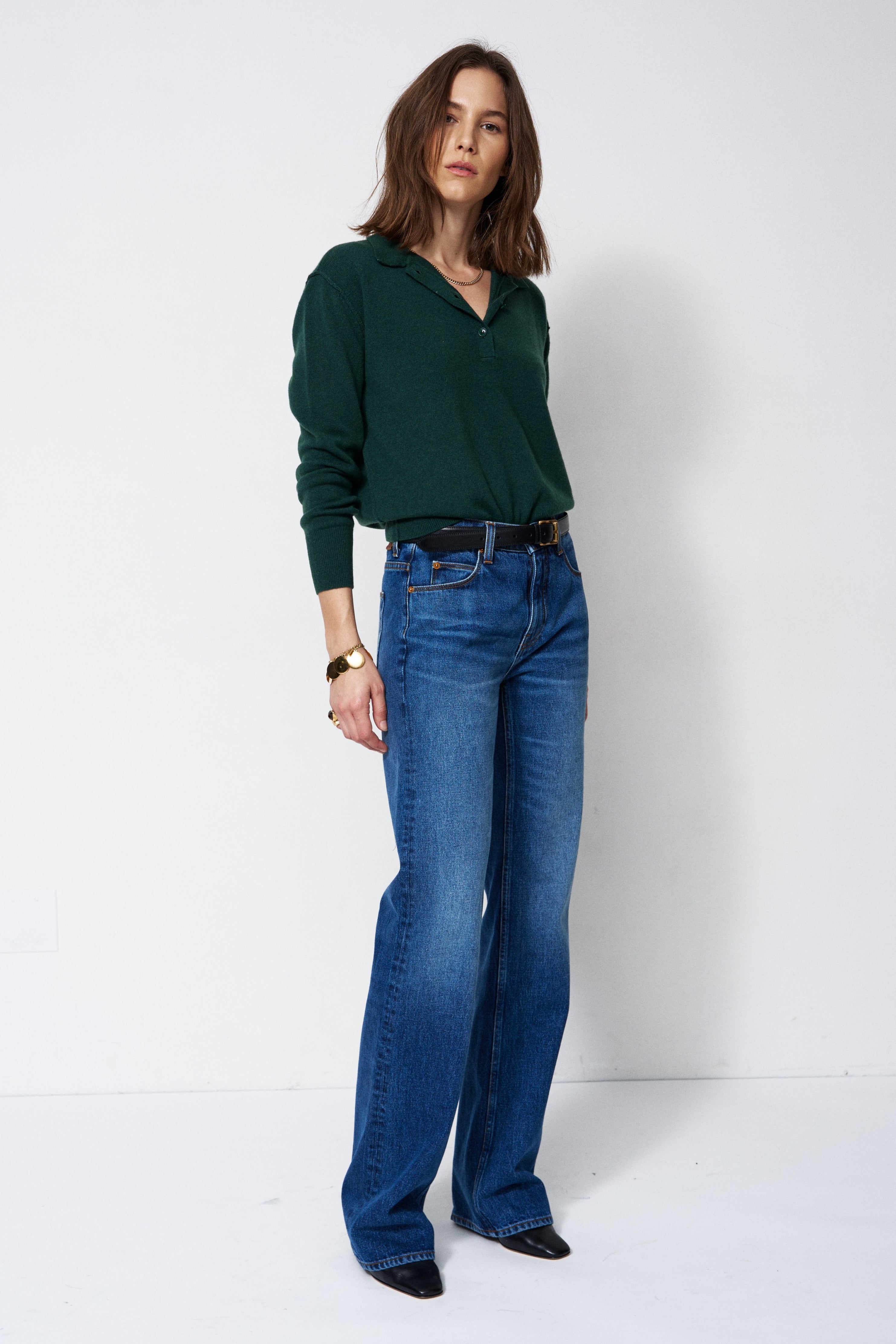 A woman modeling a dark green long-sleeve knit top and blue wide-leg jeans against a plain white studio background.