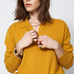 Woman wearing a mustard yellow sweater with jewelry on a plain background