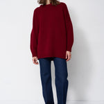 a woman in a red sweater and jeans in front of white wall