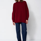 a woman in a red sweater and jeans in front of white wall