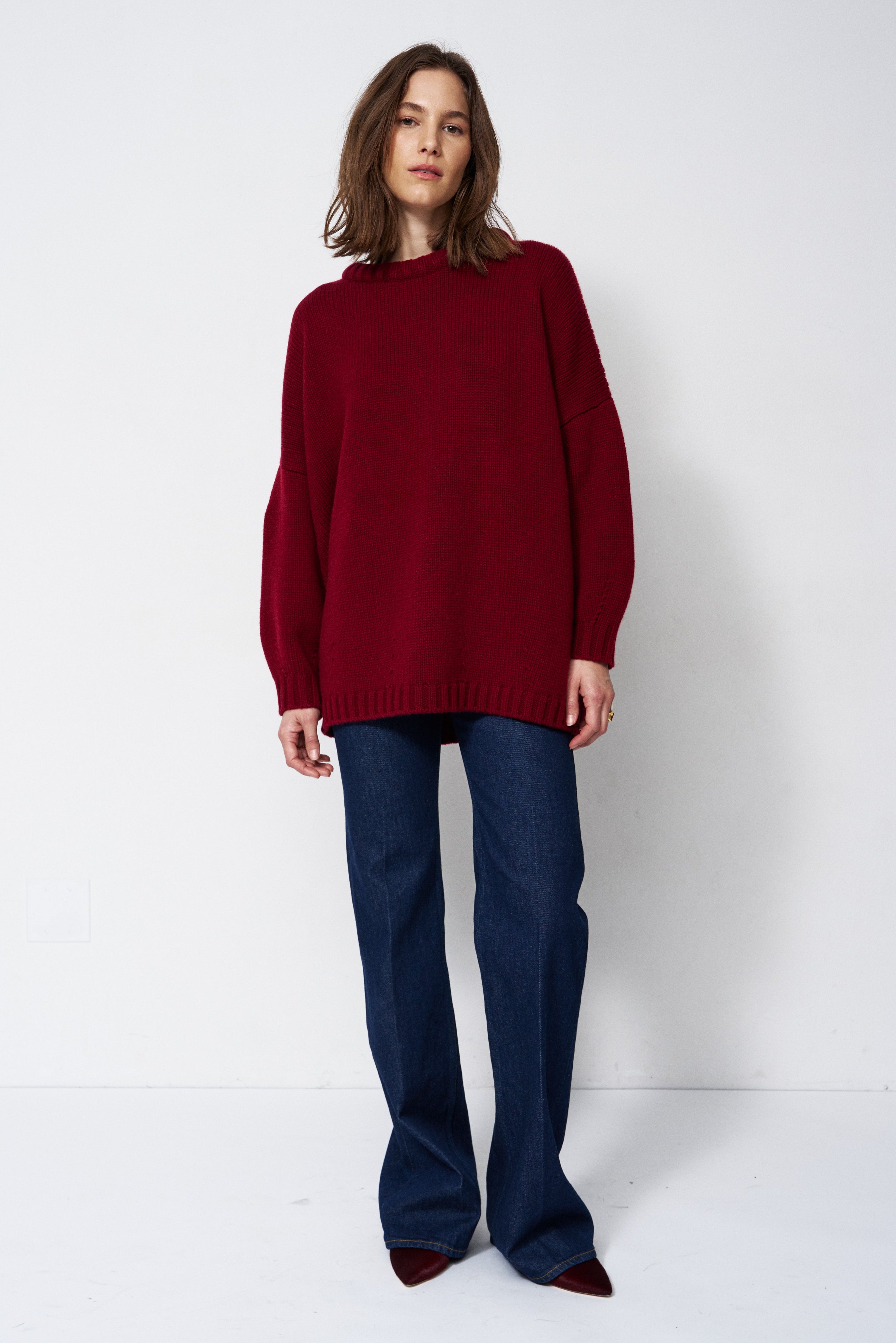 a woman in a red sweater and jeans in front of white wall