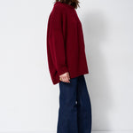 a woman in a red sweater and jeans in front of white wall