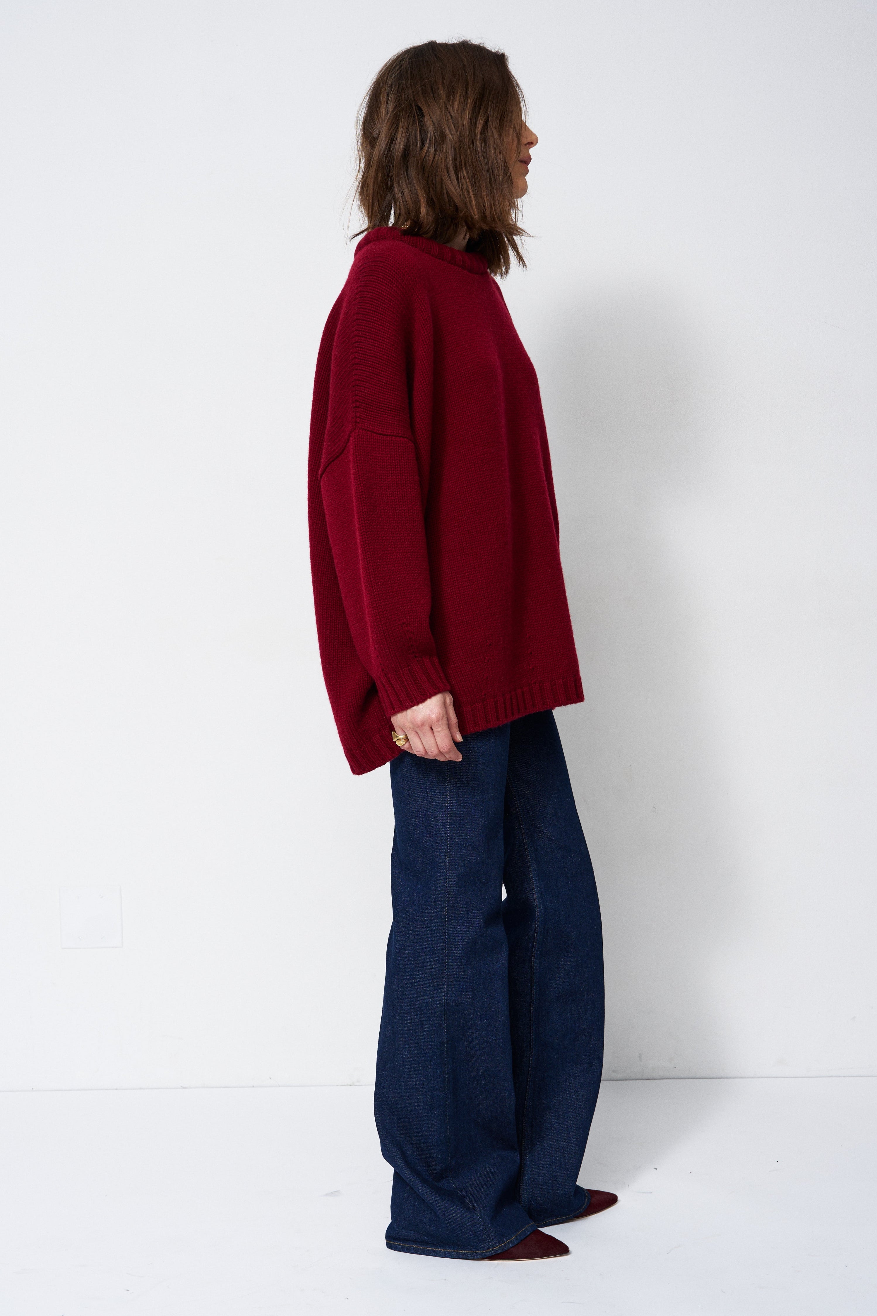 a woman in a red sweater and jeans in front of white wall