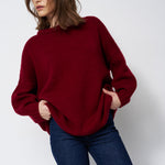 a woman in a red sweater and jeans in front of white wall