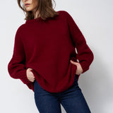 a woman in a red sweater and jeans in front of white wall