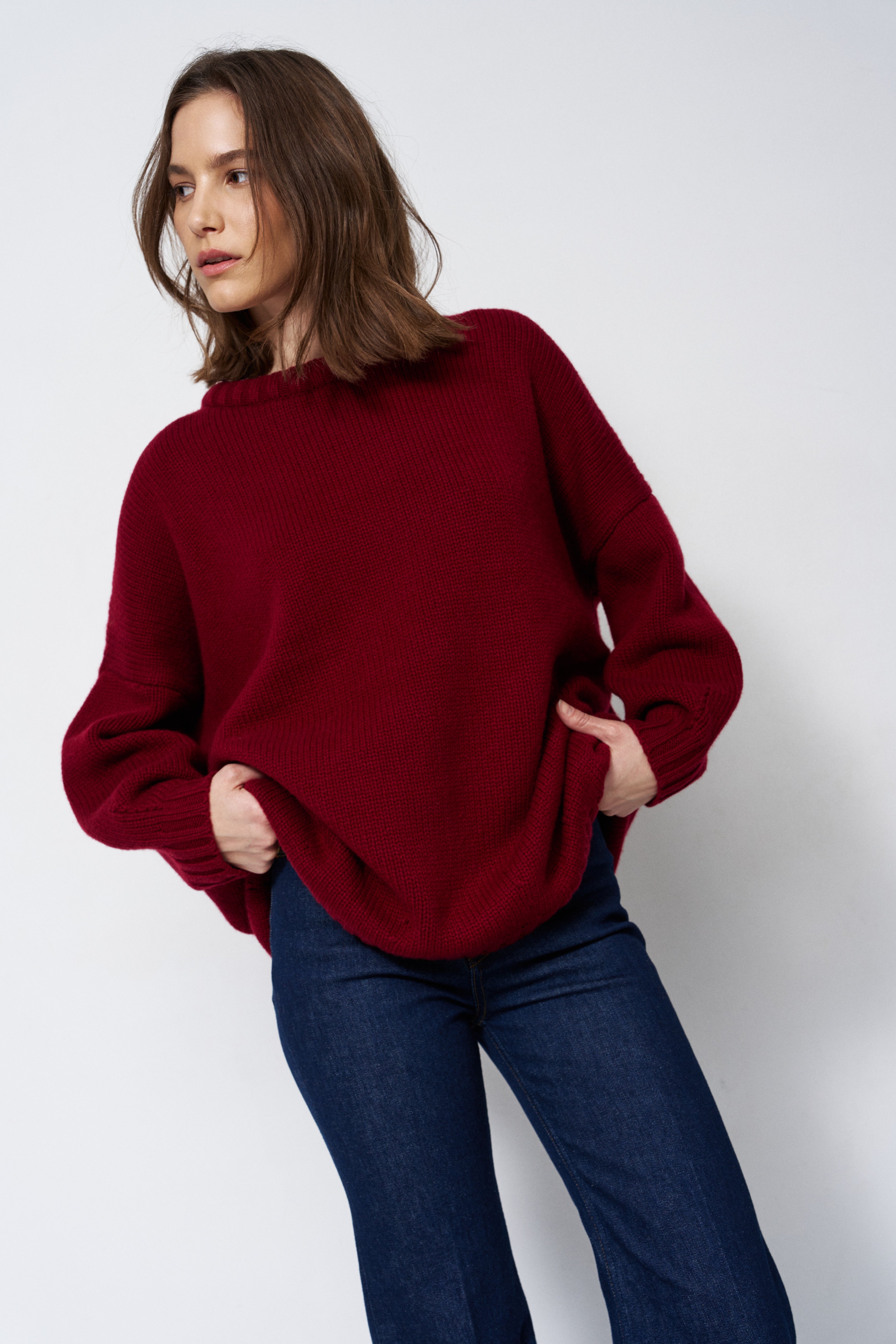 a woman in a red sweater and jeans in front of white wall